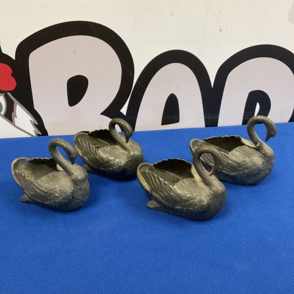 Set of four antique pewter swans displayed on a dark surface.
