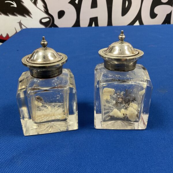 Antique silver plate topped cut glass inkwells on a dark surface.