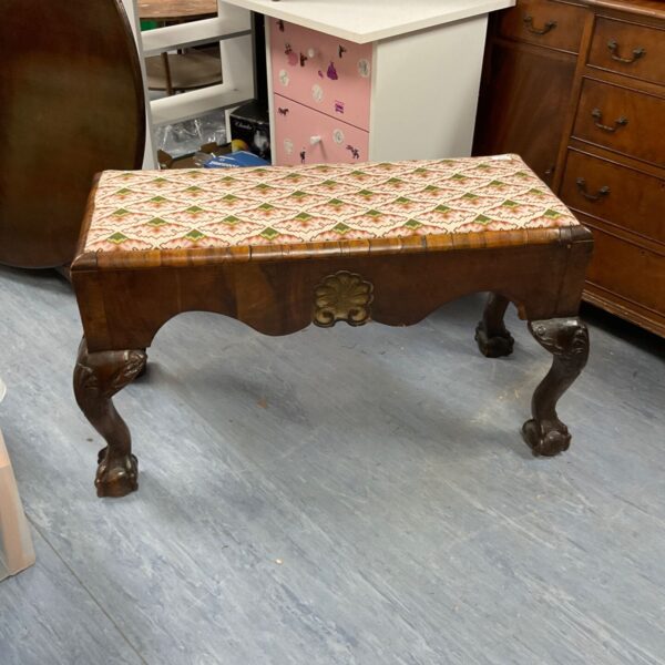 Antique upholstered long stool with carved wooden legs.
