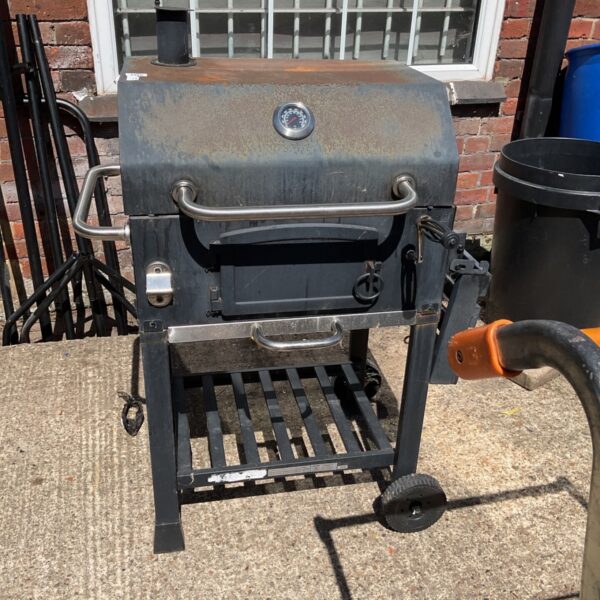 Side view of a used BBQ smoker oven with thermometer.