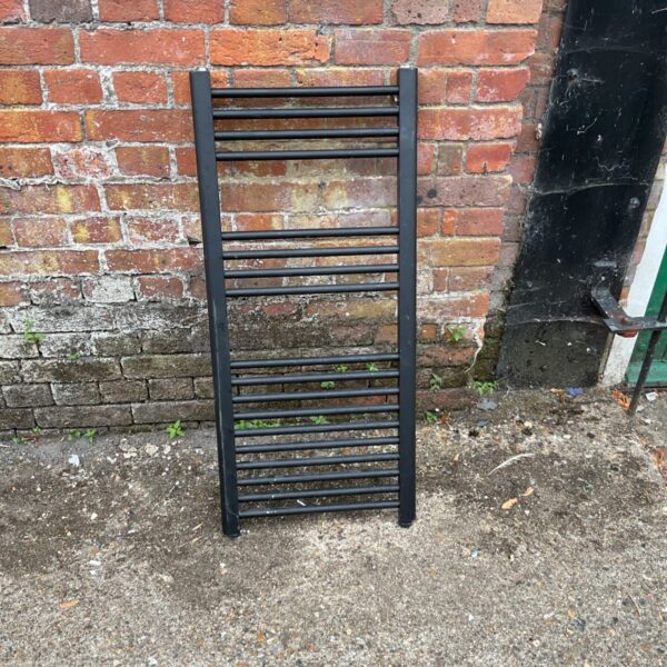 Black bathroom towel rail against a brick wall.