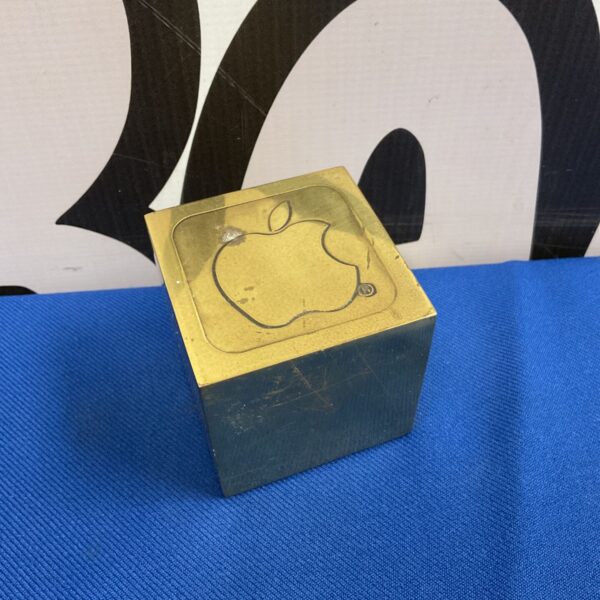 Vintage brass apple Macintosh paperweight on a dark surface.