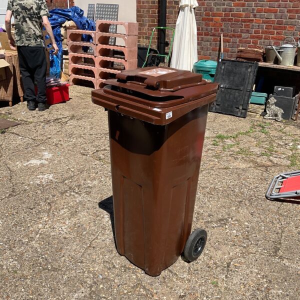 Brown food waste recycling bin with wheels in a garden setting.