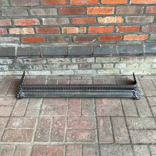 Antique cast iron fireplace fender with repeating decorative pattern.