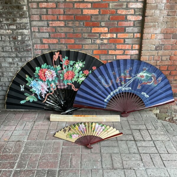 Vintage Chinese fans with floral and dragon designs displayed against a brick wall.