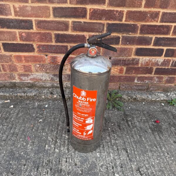 Vintage Chubb fire extinguisher against brick wall.