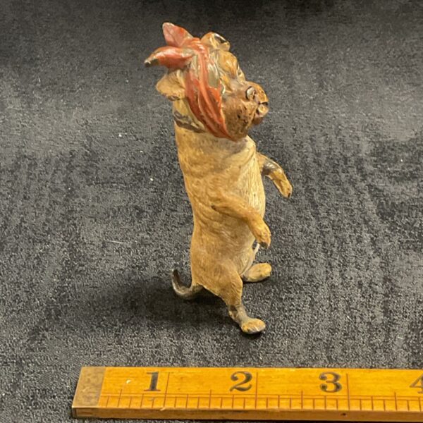 Antique cold-painted metal dog figurine with red head covering.