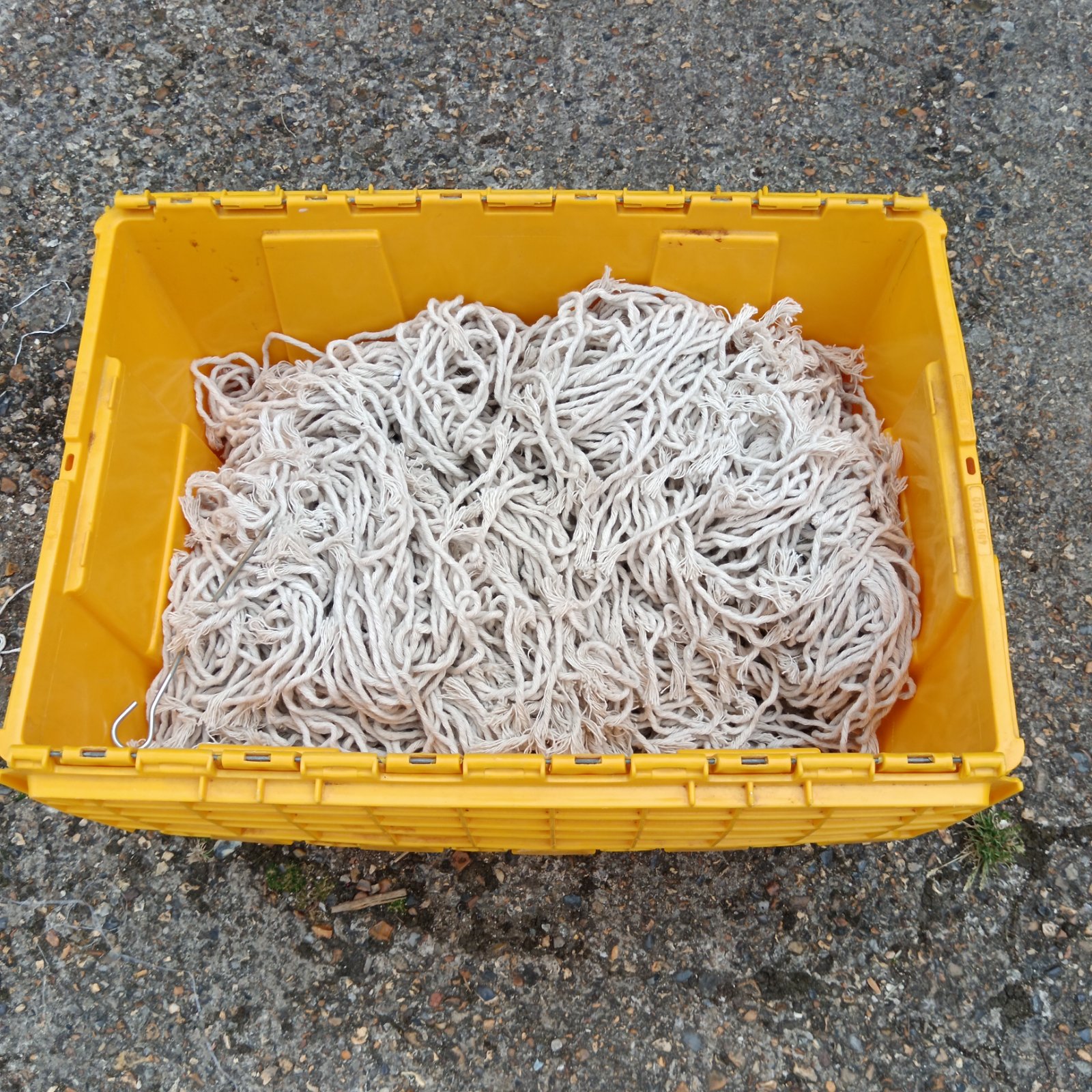 Yellow crate filled with bulk cotton mop heads for cleaning.