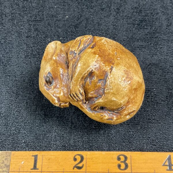 Ceramic dormouse figurine with ruler for scale.
