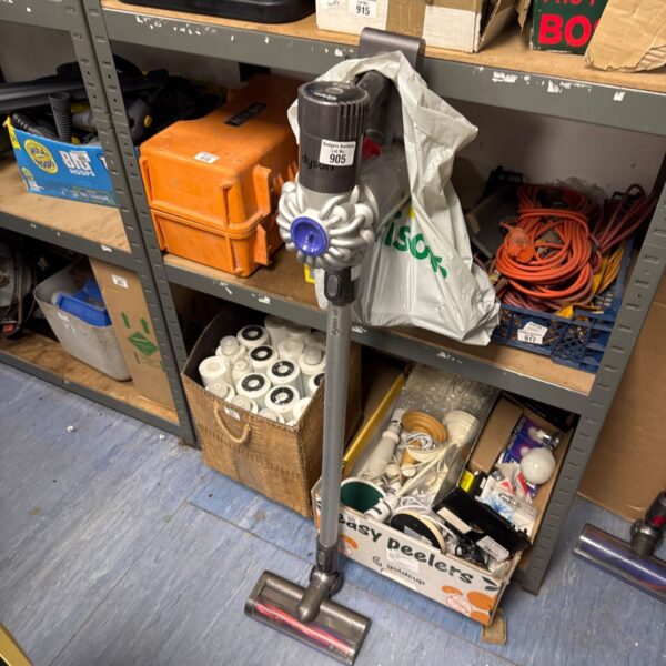 Dyson V6 cordless vacuum cleaner on a shelf with accessories.