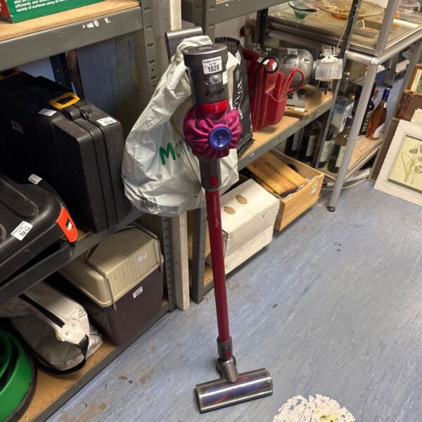 Dyson V7 Total Clean cordless vacuum with accessories in a cluttered space.