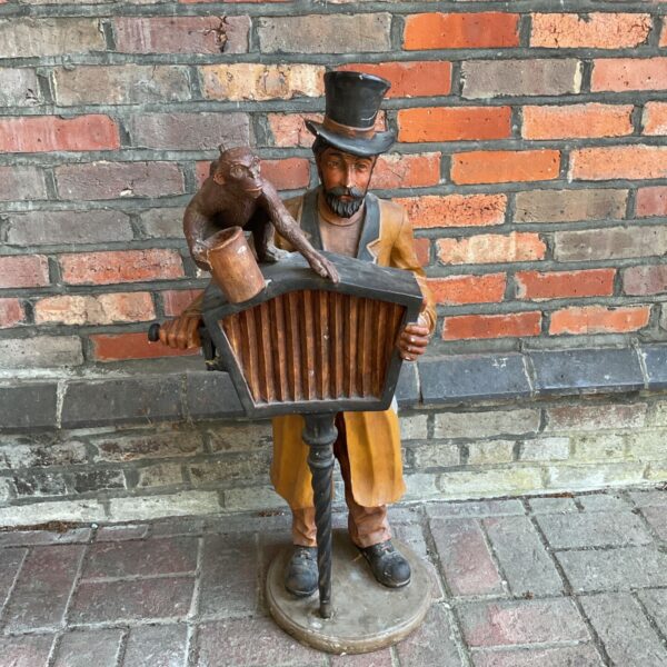 Large fibreglass organ grinder statue with monkey in garden setting.