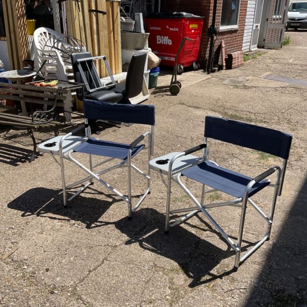 Two blue folding camping chairs with side tables in a garden setting.