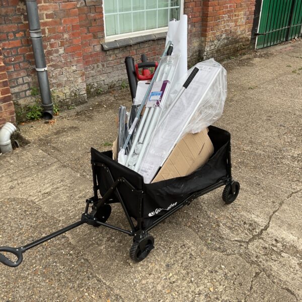 Black folding garden cart loaded with shower parts and DIY materials.