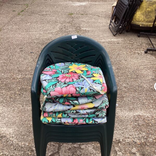 Stack of four green garden chairs with floral cushions.