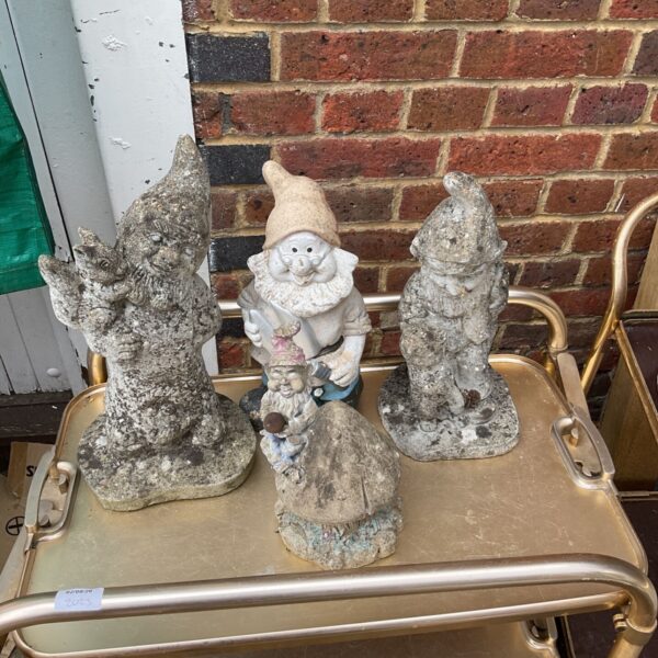 Collection of three weathered garden gnomes in a garden setting.