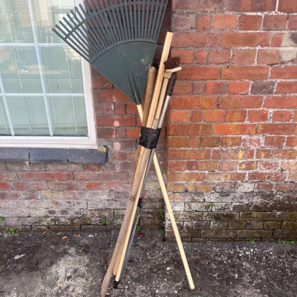 Green plastic rake with wooden handle, part of a garden tool lot.