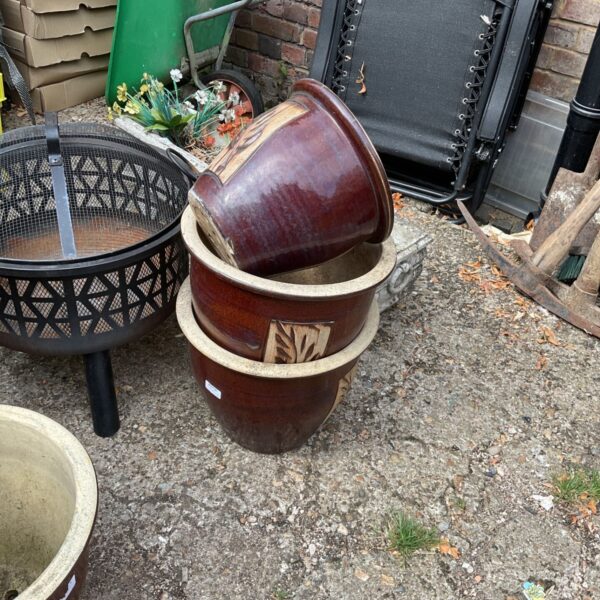 Lot of three glazed terracotta garden planters in a garden setting.