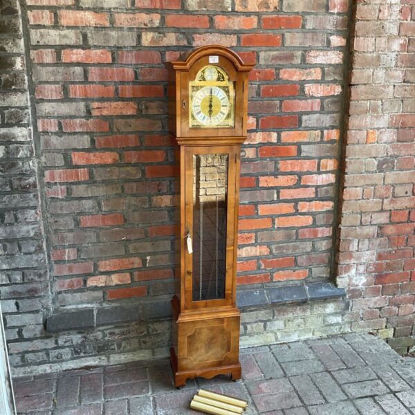 Antique yew wood grandfather clock against brick wall.