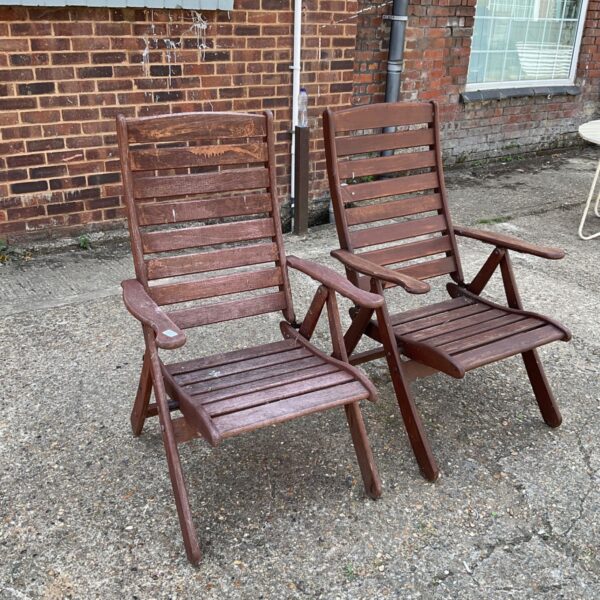 Two hardwood reclining garden chairs in a garden setting.