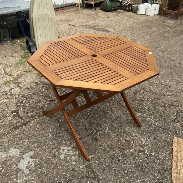 Hexagonal wooden garden table with a folding frame in a garden setting.