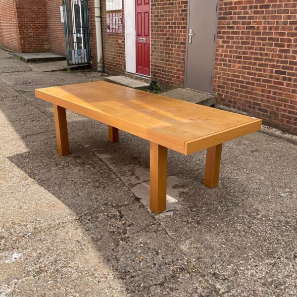 Light oak dining table positioned outside a brick building.