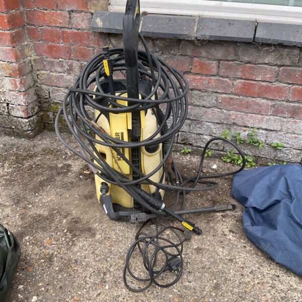 Yellow Kärcher pressure washer with hose coiled nearby.