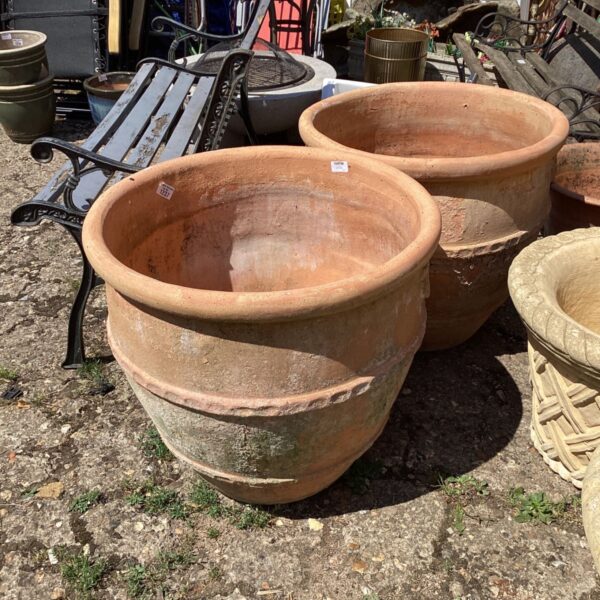 Pair of large terracotta clay planters in a garden setting.