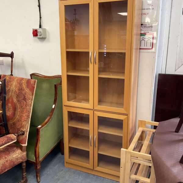 Light oak four door cabinet with glazed doors for display and storage.