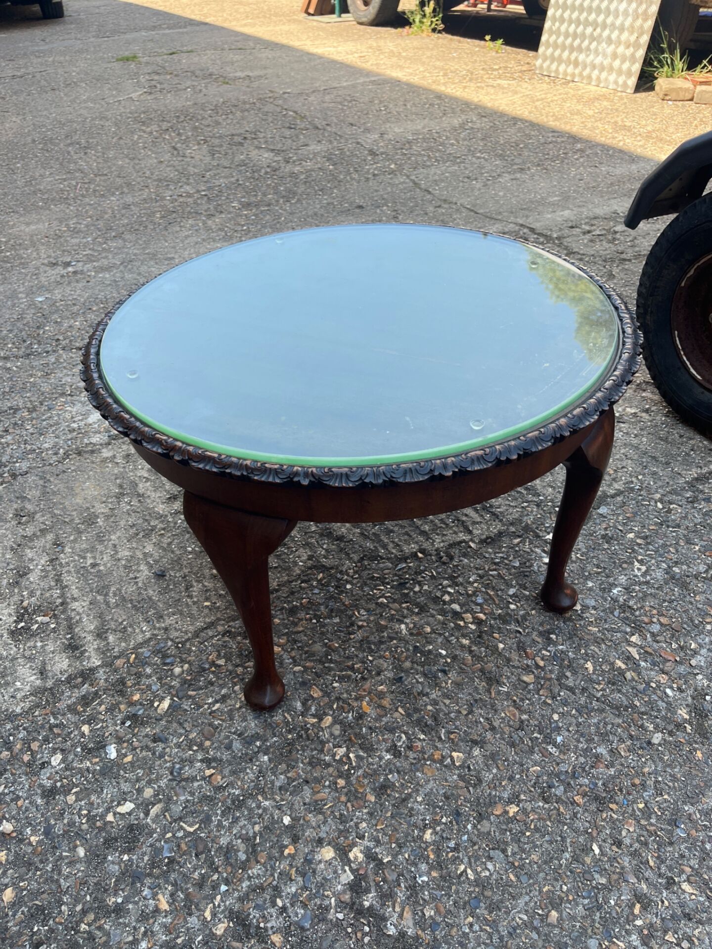 647 vintage pie crust magazine table features a round glass top set within a carved mahogany frame and is supported by four cabriole legs ending in carved ball-and-claw feet.