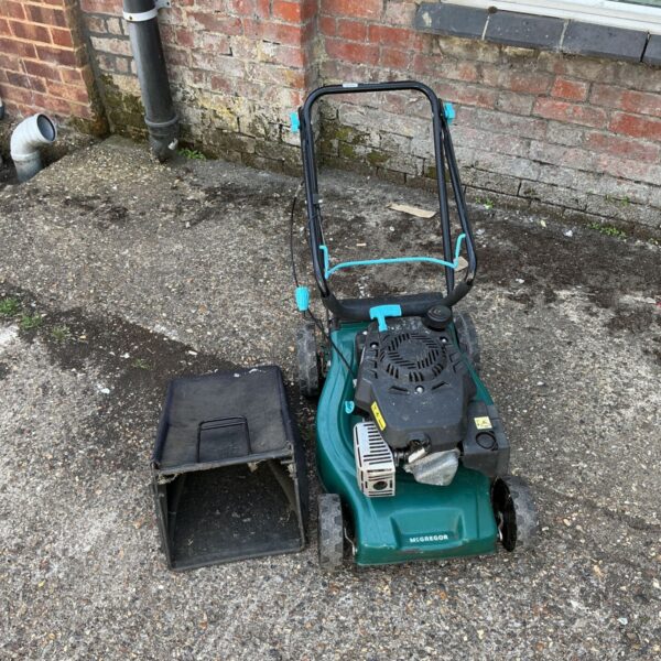 Side view of a used McGregor petrol lawnmower in a garden.