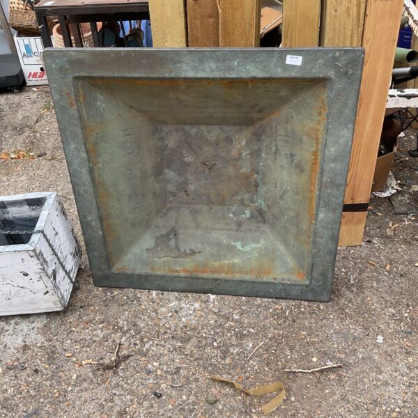 Weathered square metal fire pit for outdoor garden use.