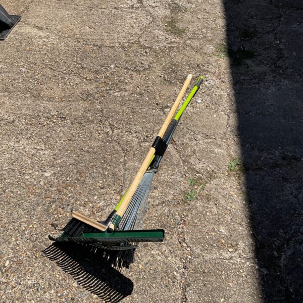 Metal lawn rake with wooden handle for garden cleanup.