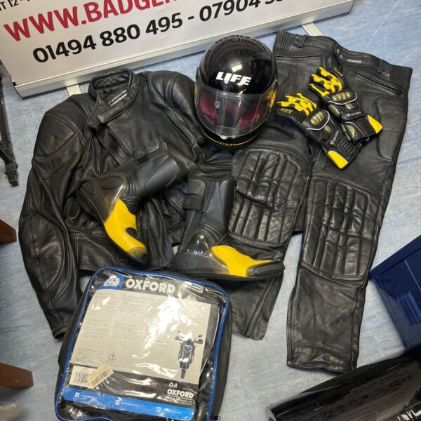 Motorcycle leather suit ensemble including jacket, trousers, helmet, and gloves.