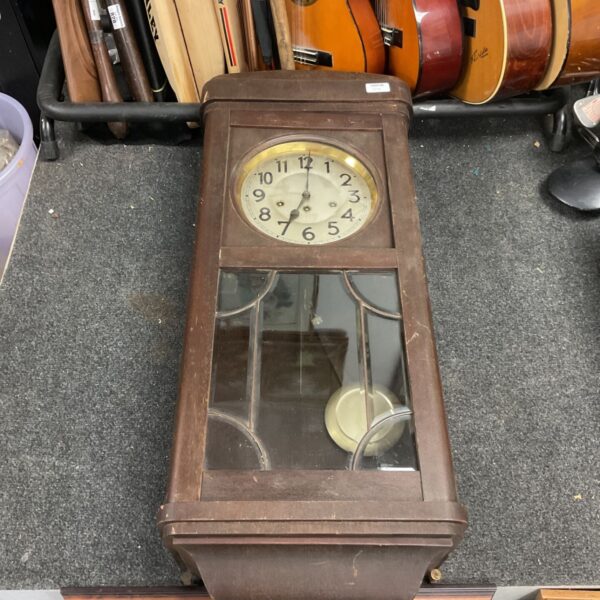 Large antique oak chiming wall clock with pendulum displayed indoors.