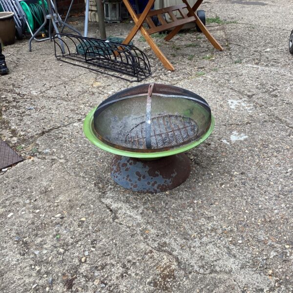 Rusty portable fire pit in a garden setting.