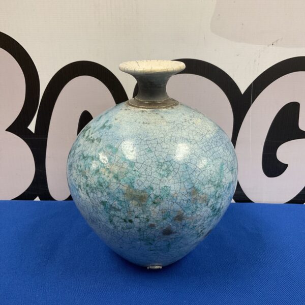 Turquoise raku vase with crackle glaze on a blue surface.