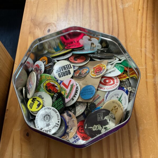 Tin of assorted retro pin badges and collectable enamel pins.