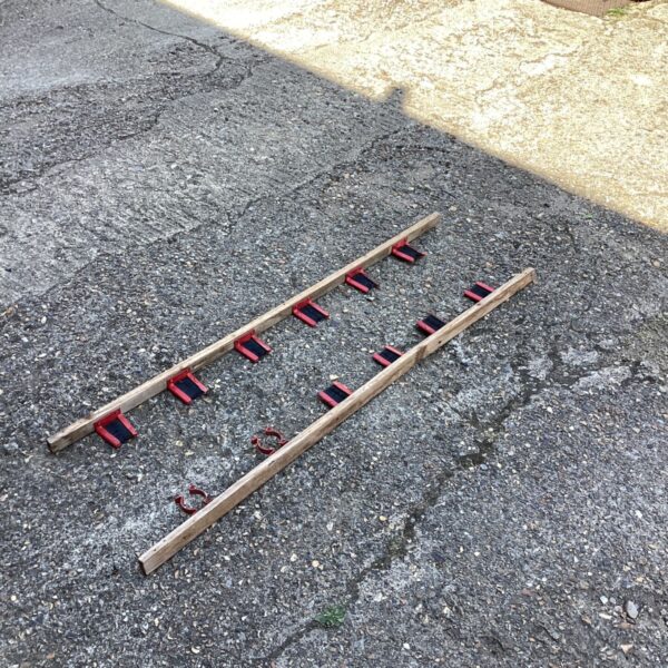 Pair of wooden shed tool hangers with red hooks.