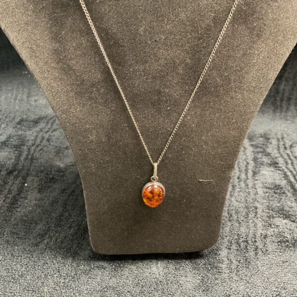 Close-up of silver pendant necklace with amber gemstone.