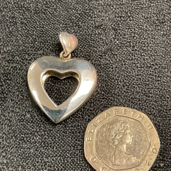 Silver Celtic heart pendant displayed with a coin for scale.