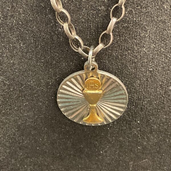 Close-up of silver necklace with JHS chalice pendant.