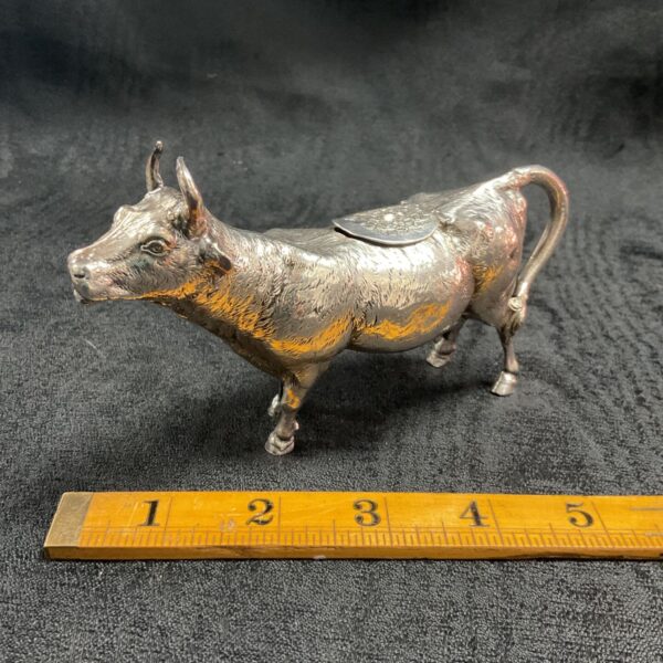 Antique silver cow creamer with ruler for scale.