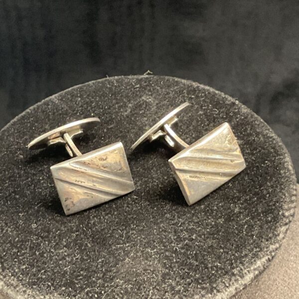 Vintage silver cufflinks with a linear design on a dark background.