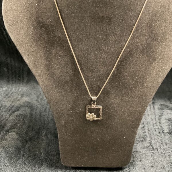 Close-up of silver daisy pendant on snake chain necklace.
