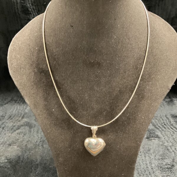 Silver heart locket necklace displayed on a mannequin.
