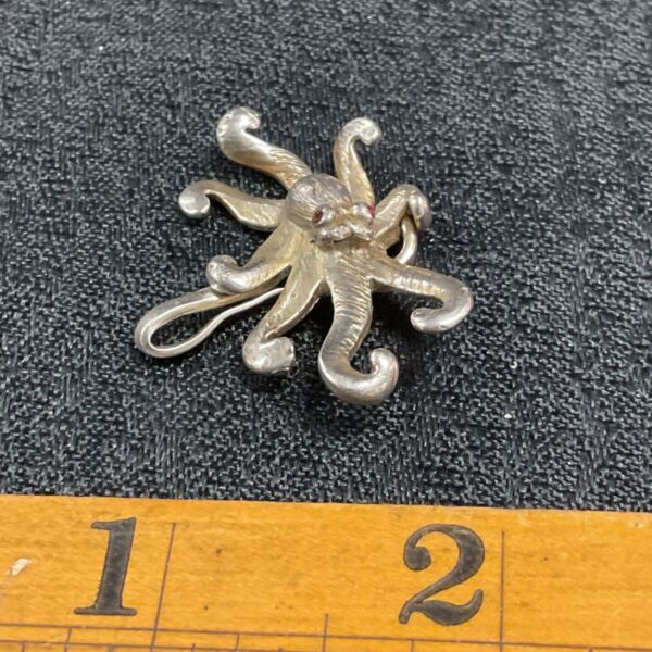 Detailed silver octopus pendant with red stone eyes.
