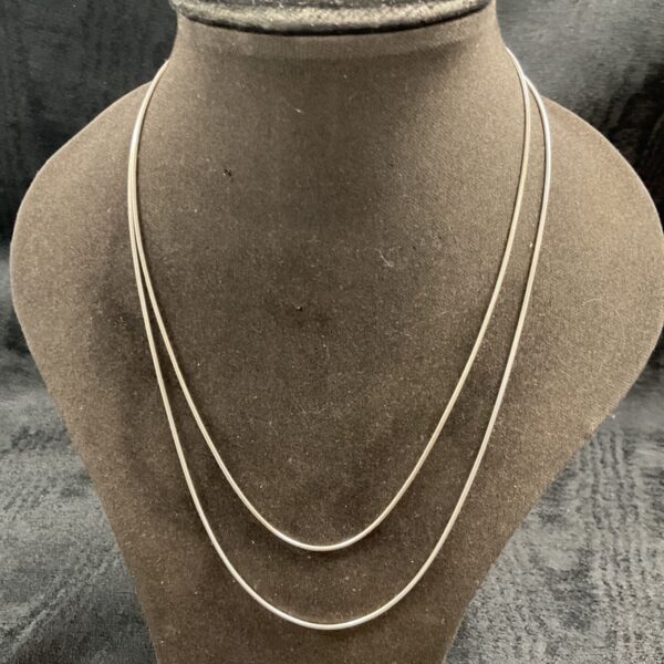 Layered silver snake chain necklaces on display.