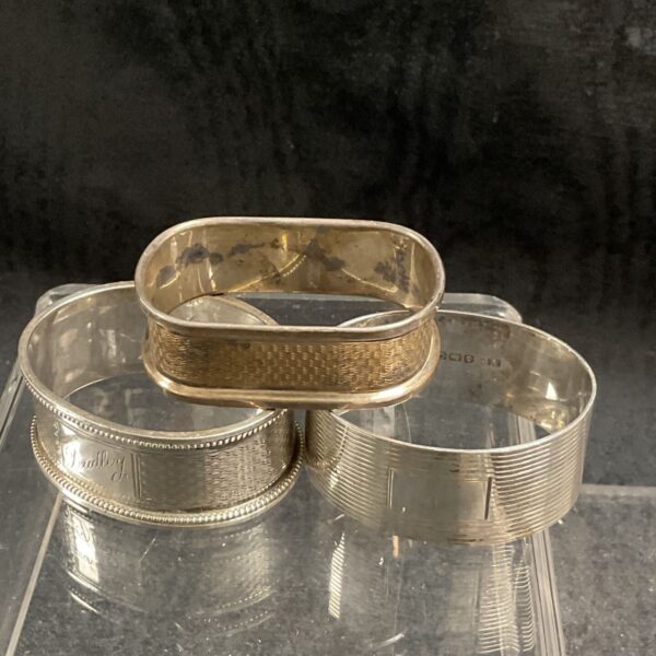 Group of antique sterling silver napkin rings with varied designs.
