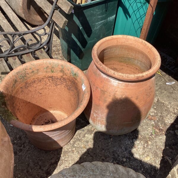 Two weathered terracotta garden planters in a garden setting.